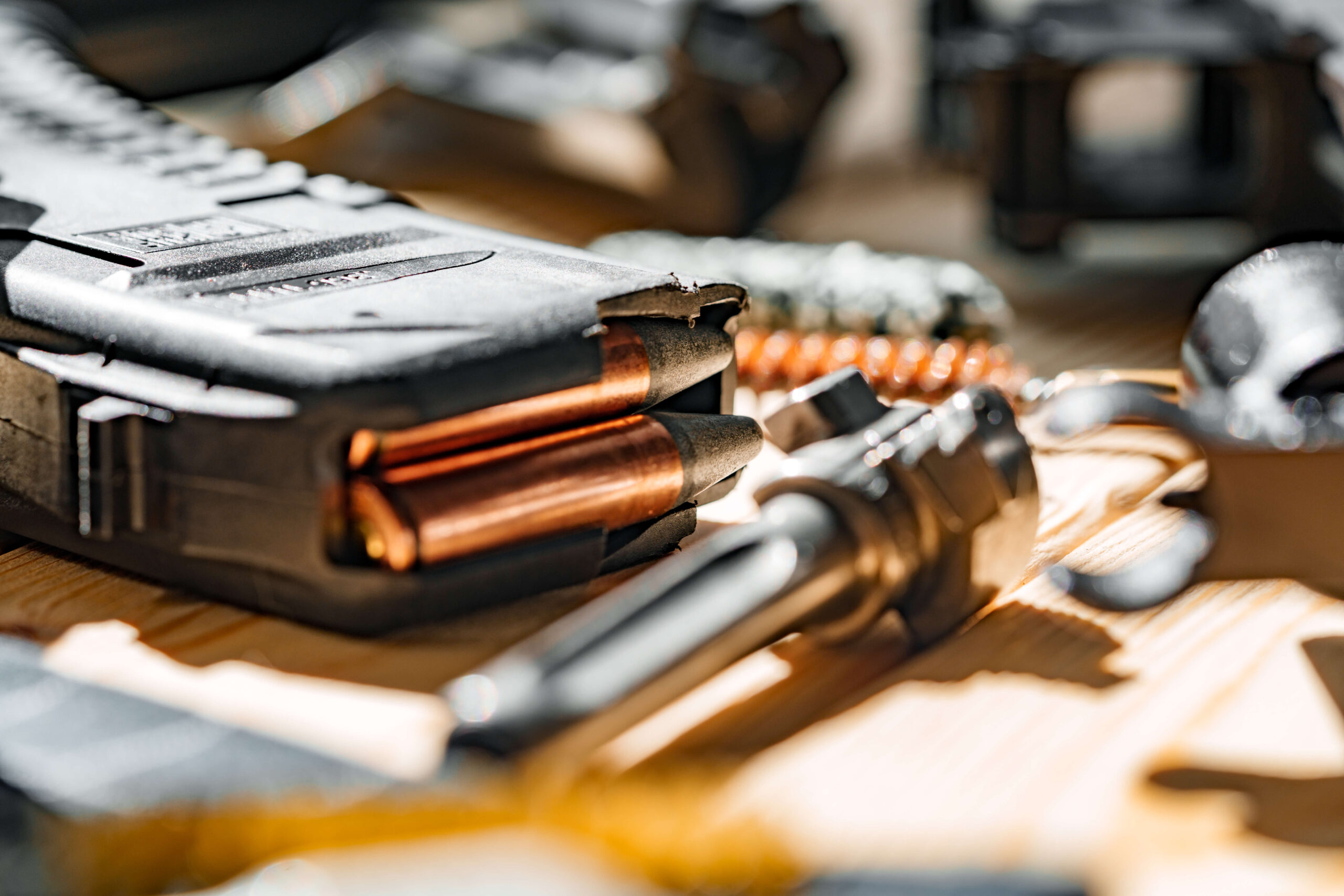 Close-up image of bullets partially loaded into a magazine, placed on a wooden surface with other firearm components around.