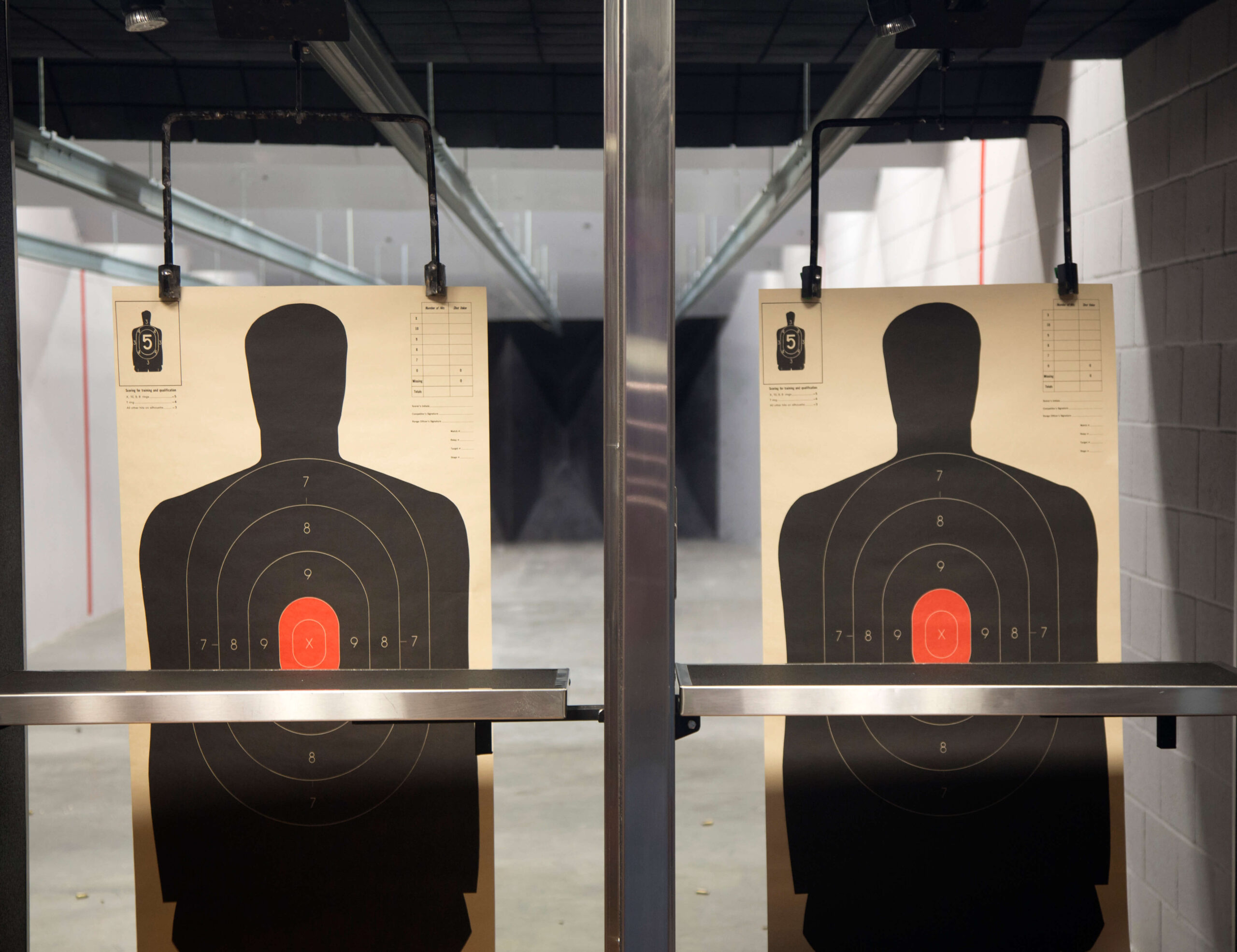 Two black silhouette shooting targets with red bullseyes are hanging at an indoor shooting range.